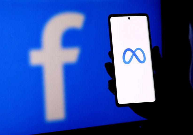 A person holding a smartphone displaying the meta logo in front of a facebook logo screen